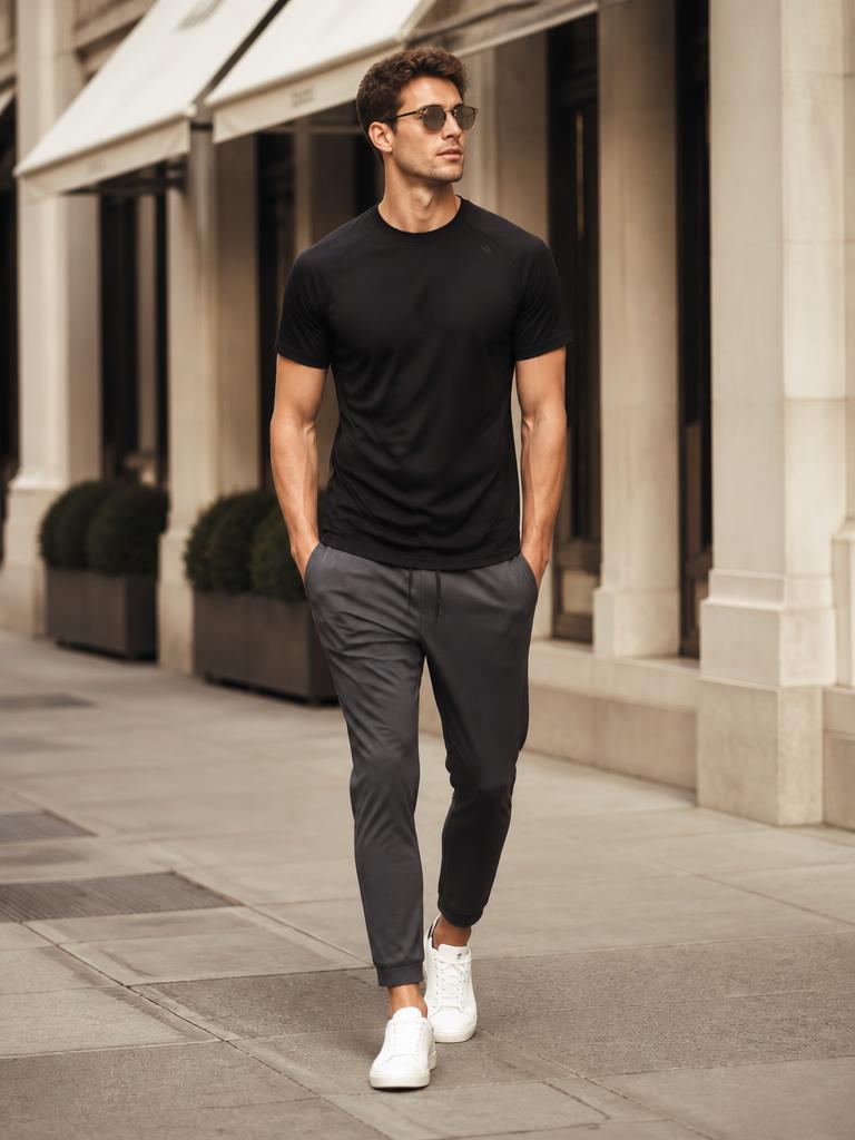 Model walking a city street in a black performance tee and charcoal joggers